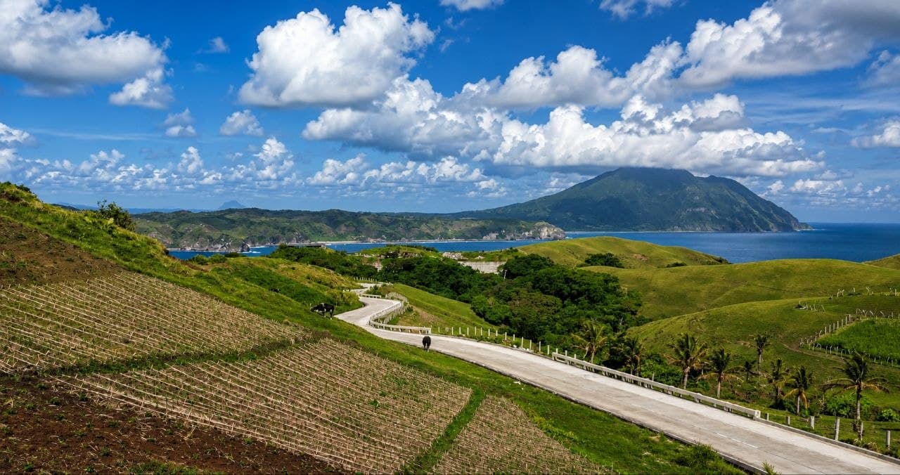 Rolling Batanes pasture overlooking a calm bay and distant mountain