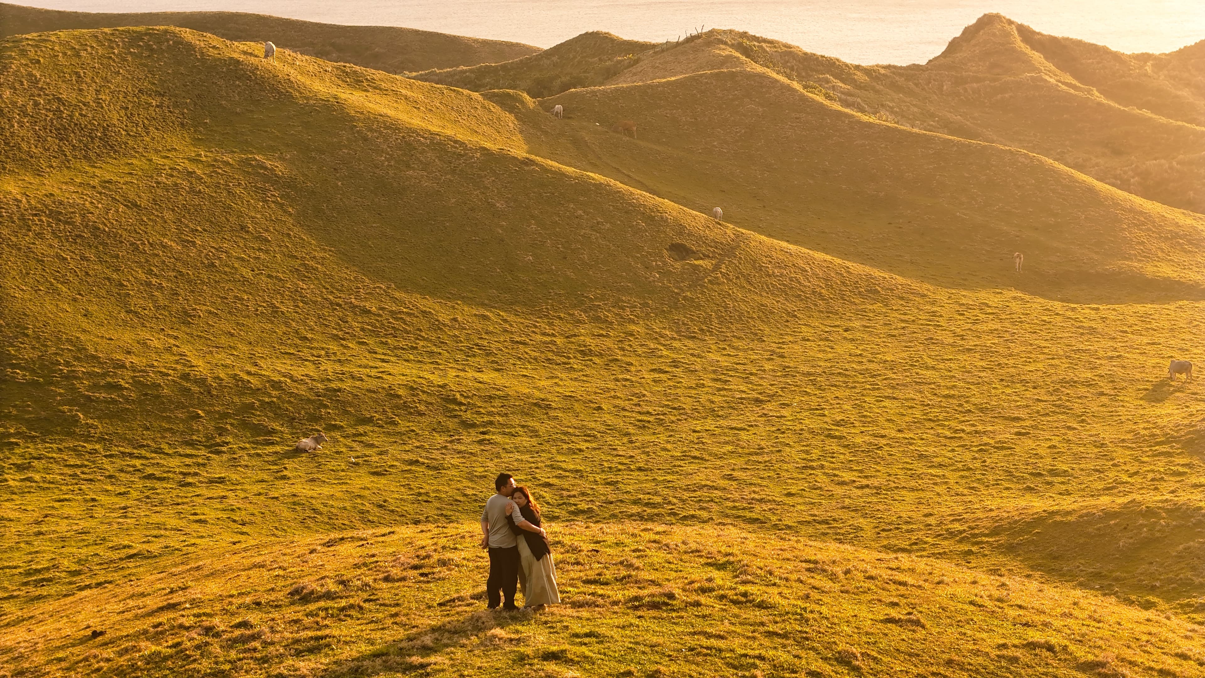 A couple standing together among sunlit rolling hills in Batanes